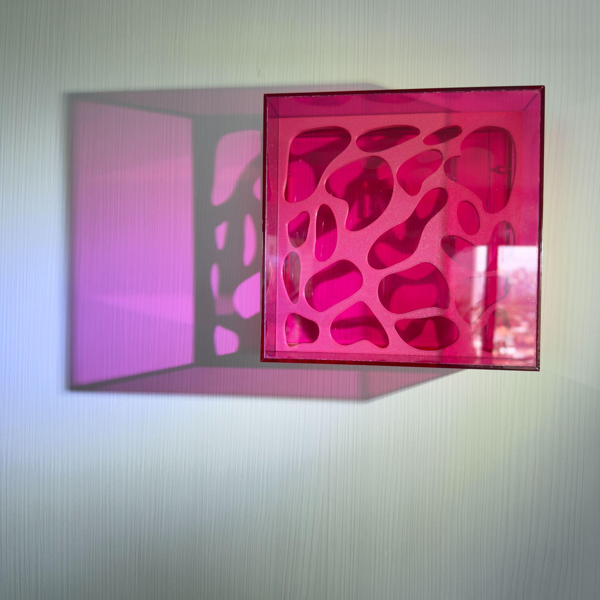 Caixa de luz rosa projetando sombra na parede