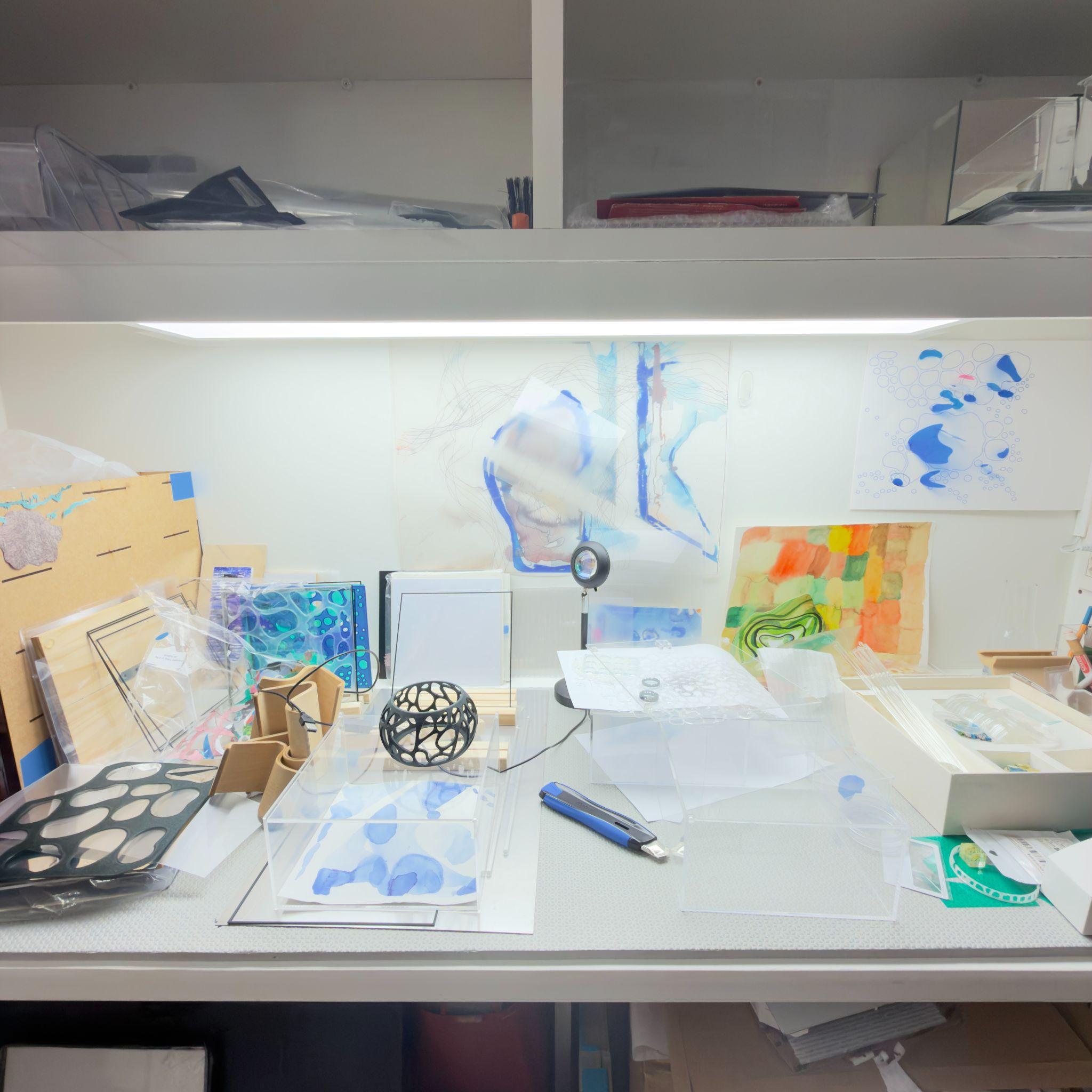 Mesa de ateliê com estudos em aquarela e vidro