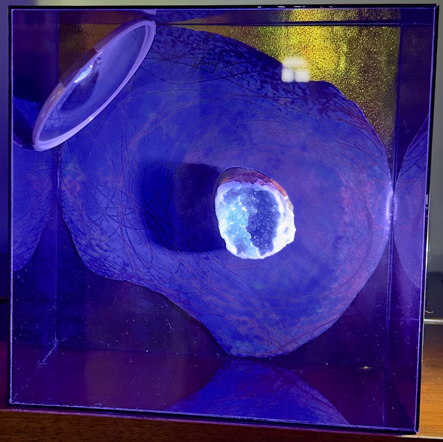 Caixa violeta com fragmento circular de madeira, lente e mineral iluminado ao centro